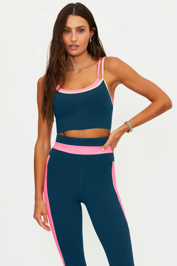 Woman wearing a navy sports bra and leggings with pink accents on a white background