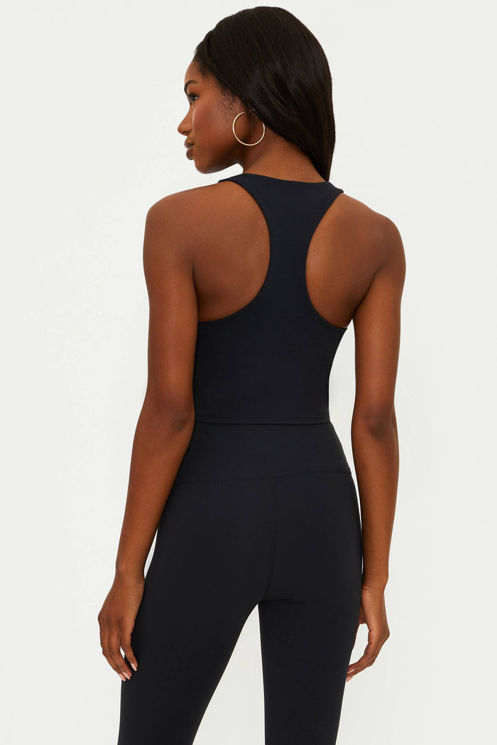 A female model wearing a black matte longline crop top with a scoop neckline and a racerback design.