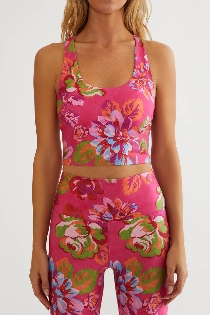 Woman wearing a bright pink floral sports bra and leggings set on a white background